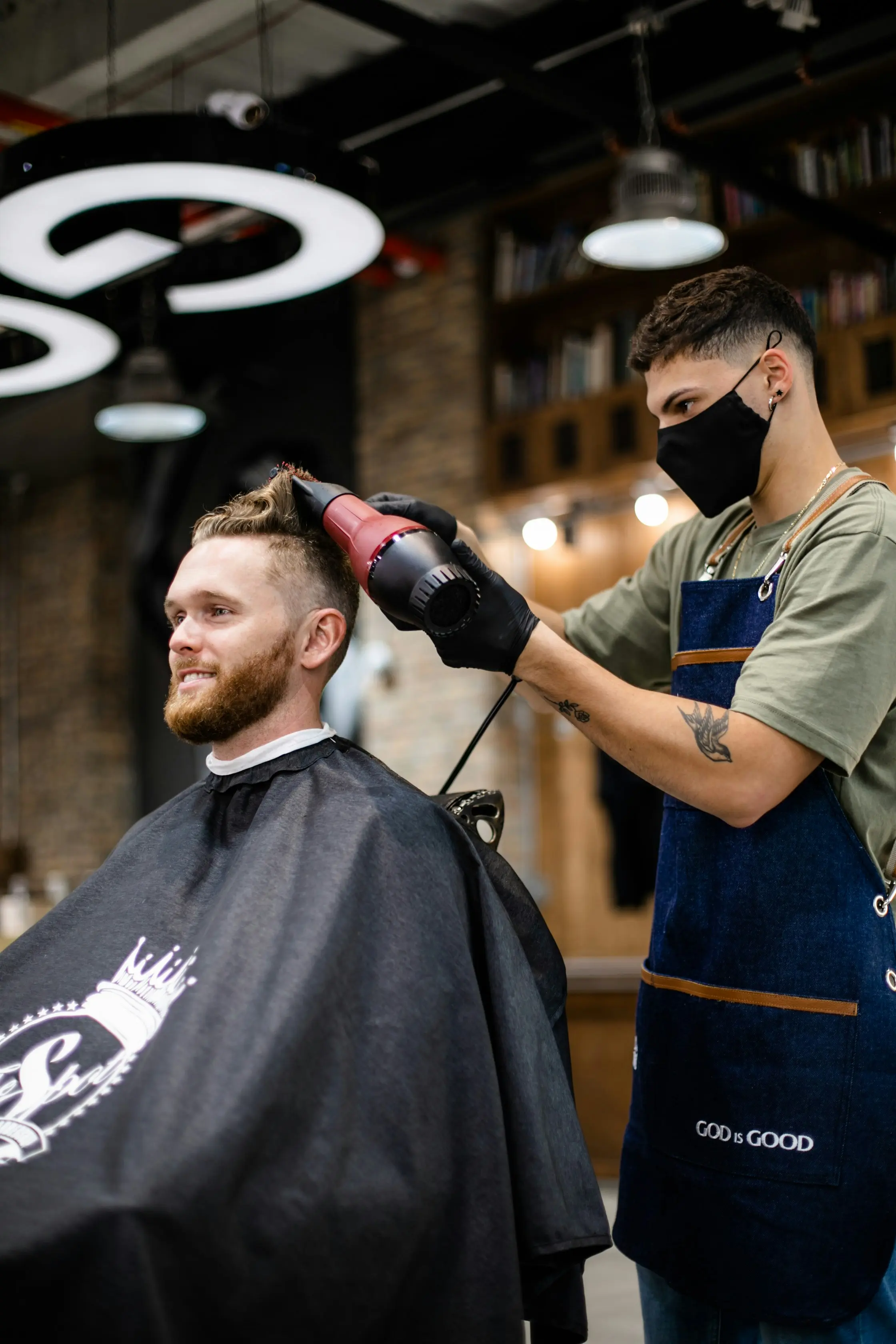 Barbeiro a cortar o cabelo de um cliente, com azulejos azuis e brancos na parede